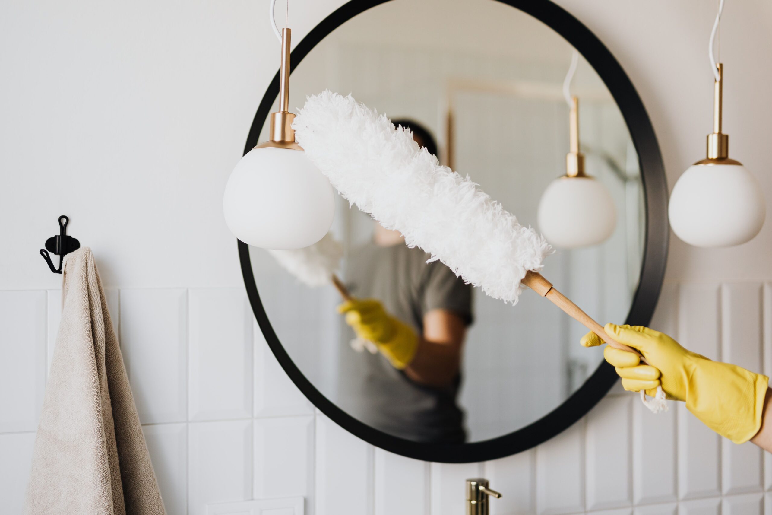 Cleaner dusting a bathroom mirror